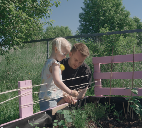 Lars Moe viser en liten jente noen voksende planter i et bed